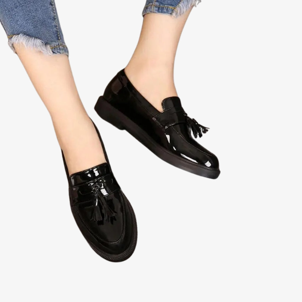 Damesloafers van zwart lakleer, elegant en glanzend. Deze schoenen zijn afgewerkt met decoratieve kwastjes op de wreef, die een klassiek en verfijnd accent geven. Hun tijdloze design past perfect bij een chique en casual look.