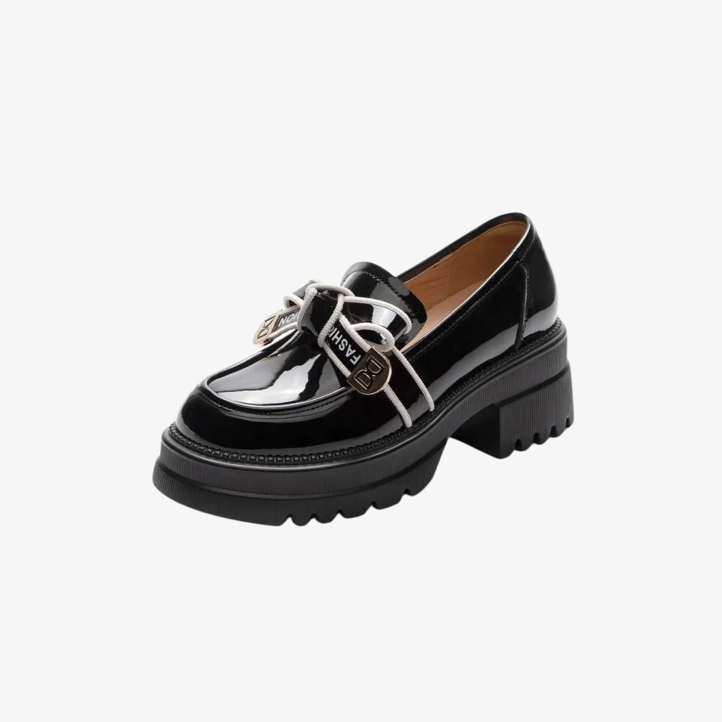 Glanzend zwarte loafers voor dames van synthetisch leer, met dikke hakken met inkepingen voor een moderne en gedurfde stijl. Een versiering met witte veters en gouden metalen ornamenten op de bovenkant geeft deze chique en comfortabele schoenen een elegante en originele touch.