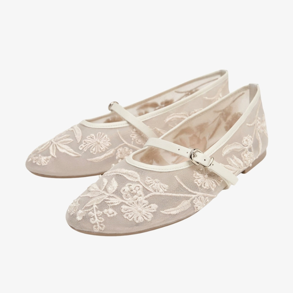 Witte ballerina loafer met bloemenborduurwerk en een bandje, op een grijze achtergrond