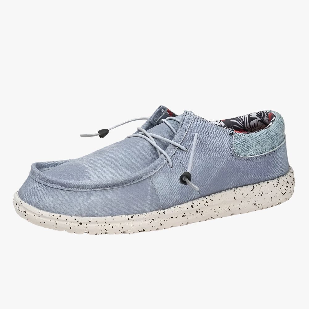 Loafers van blauwe stof met witte zolen. De stof aan de binnenkant heeft een bloemenmotief.