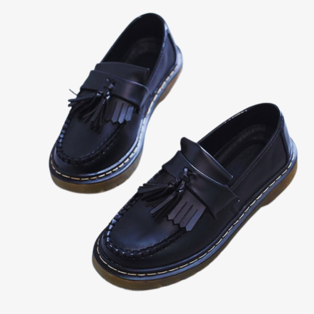 je ziet op een witte achtergrond een paar loafers met kwastjes en franjes van synthetisch leer voor dames, ze zijn zwart