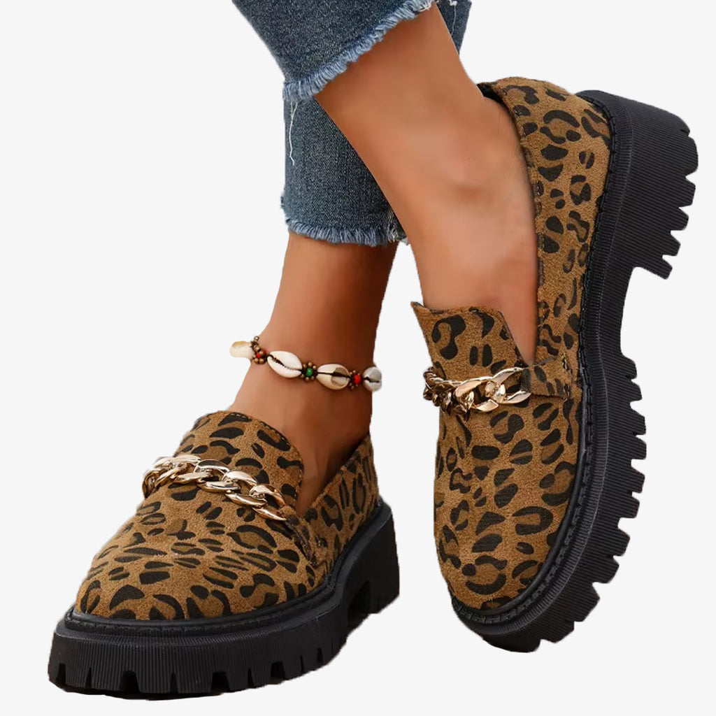 Paar loafers van luipaardsuède met plateauzool en ketting, gedragen met een jeans en een enkelbandje van schelpen