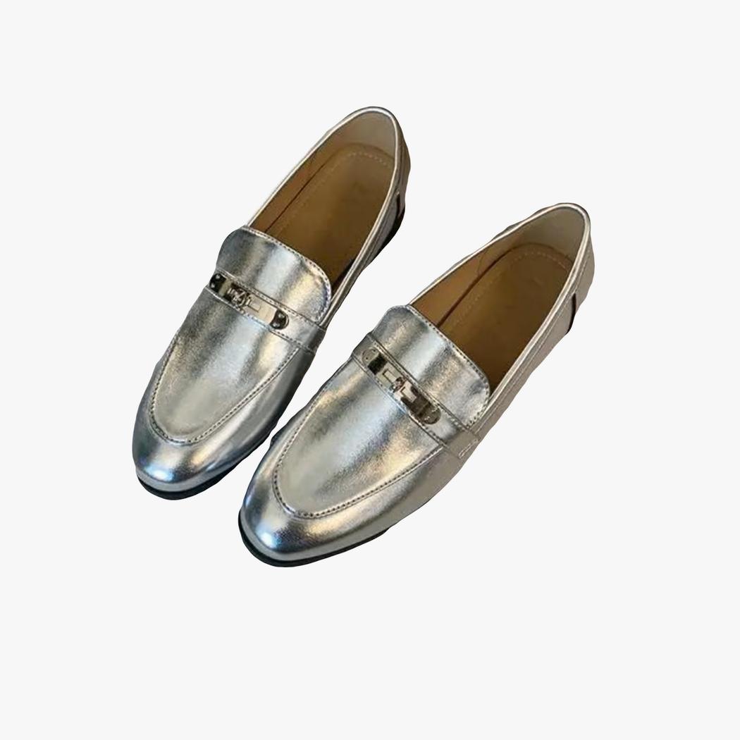 je ziet op een lichte achtergrond een paar zilveren loafers met vierkante hak voor dames