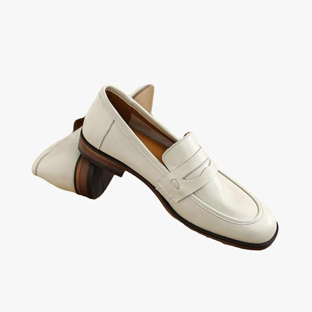 Een paar beige loafers met bruine zolen van echt leer, op een houten boomstam