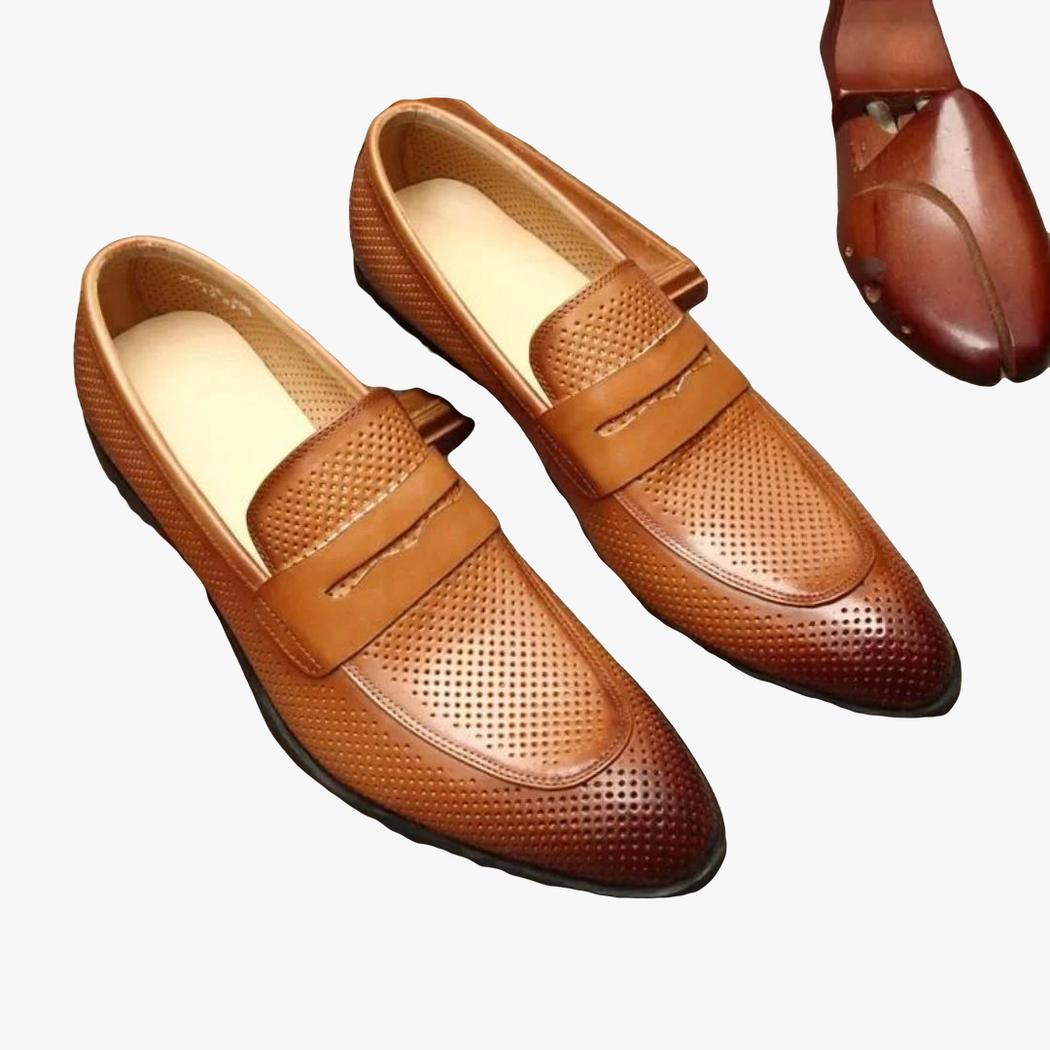 Op een grijze achtergrond zie je een paar bruine loafers met puntneus van echt leer voor heren