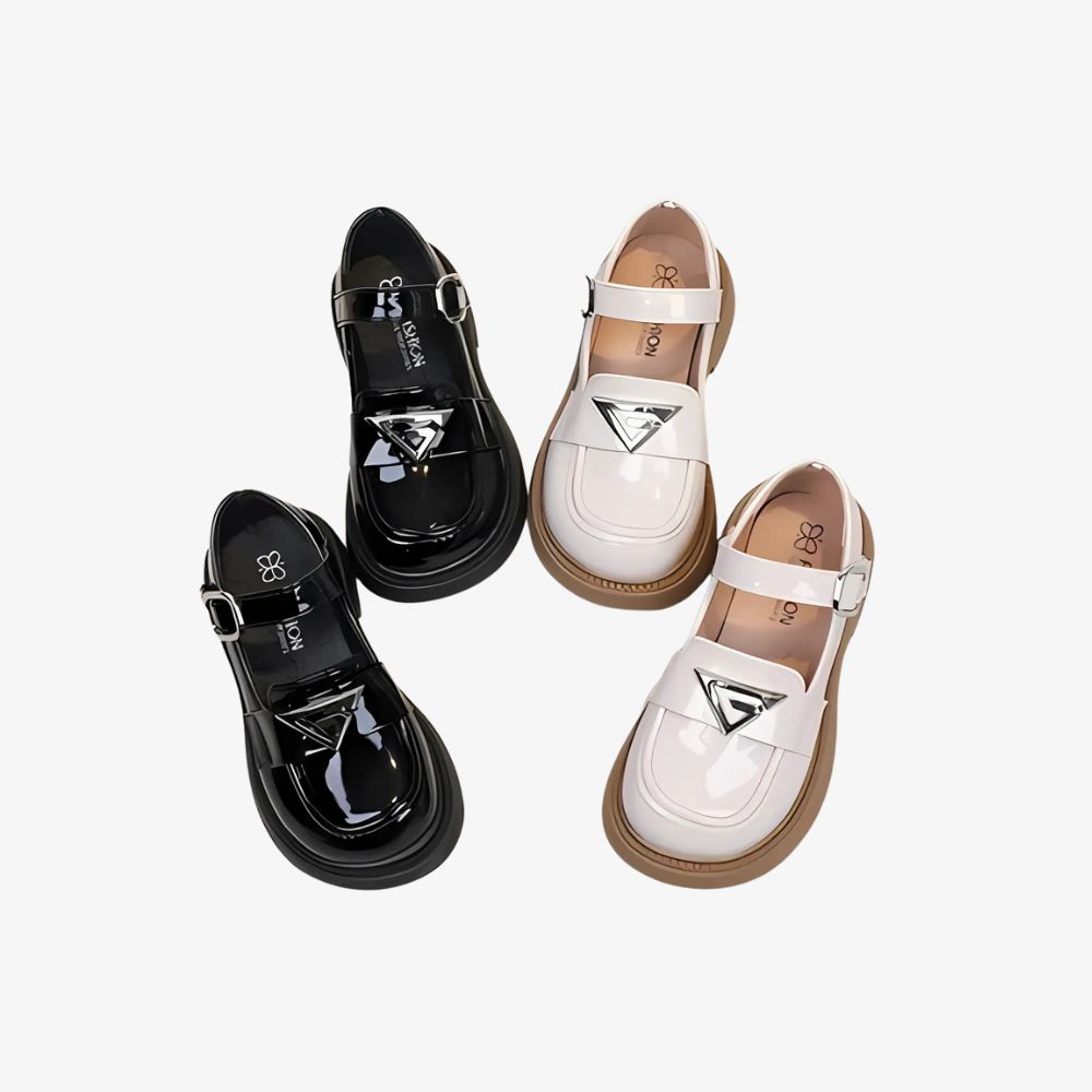 2 paar glanzende loafers in zwart en wit met zilverkleurige details, op een grijze achtergrond.
