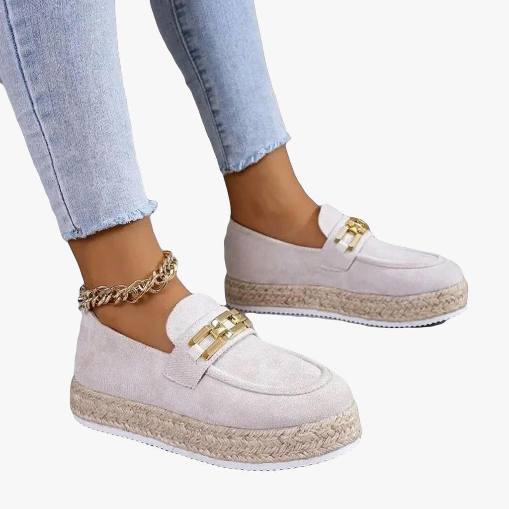 Je ziet de voeten van een vrouw in jeans die beige sleehak loafers van synthetisch suède draagt