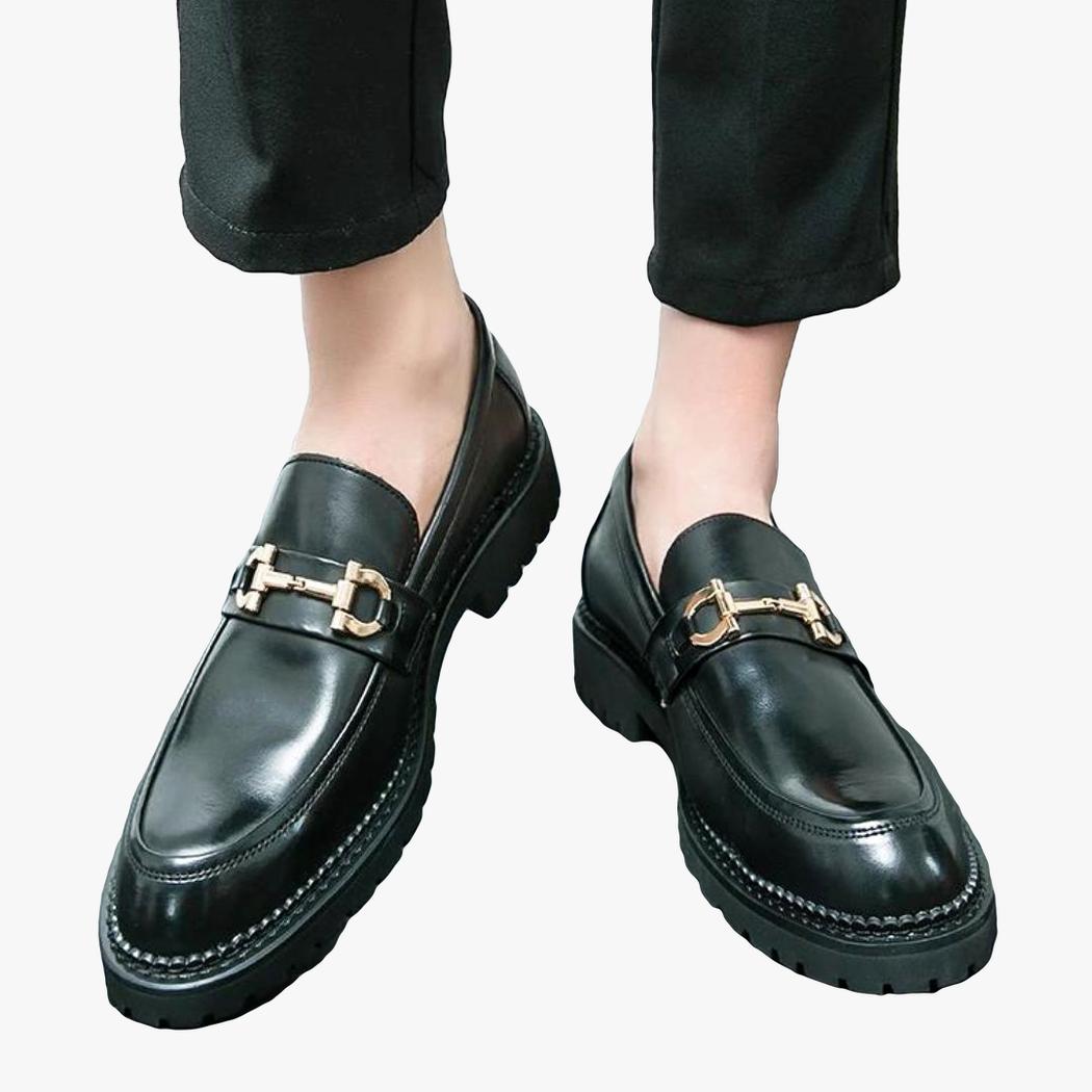 Je ziet de voeten van een man die zwarte loafers met metalen gesp van synthetisch leer voor heren draagt