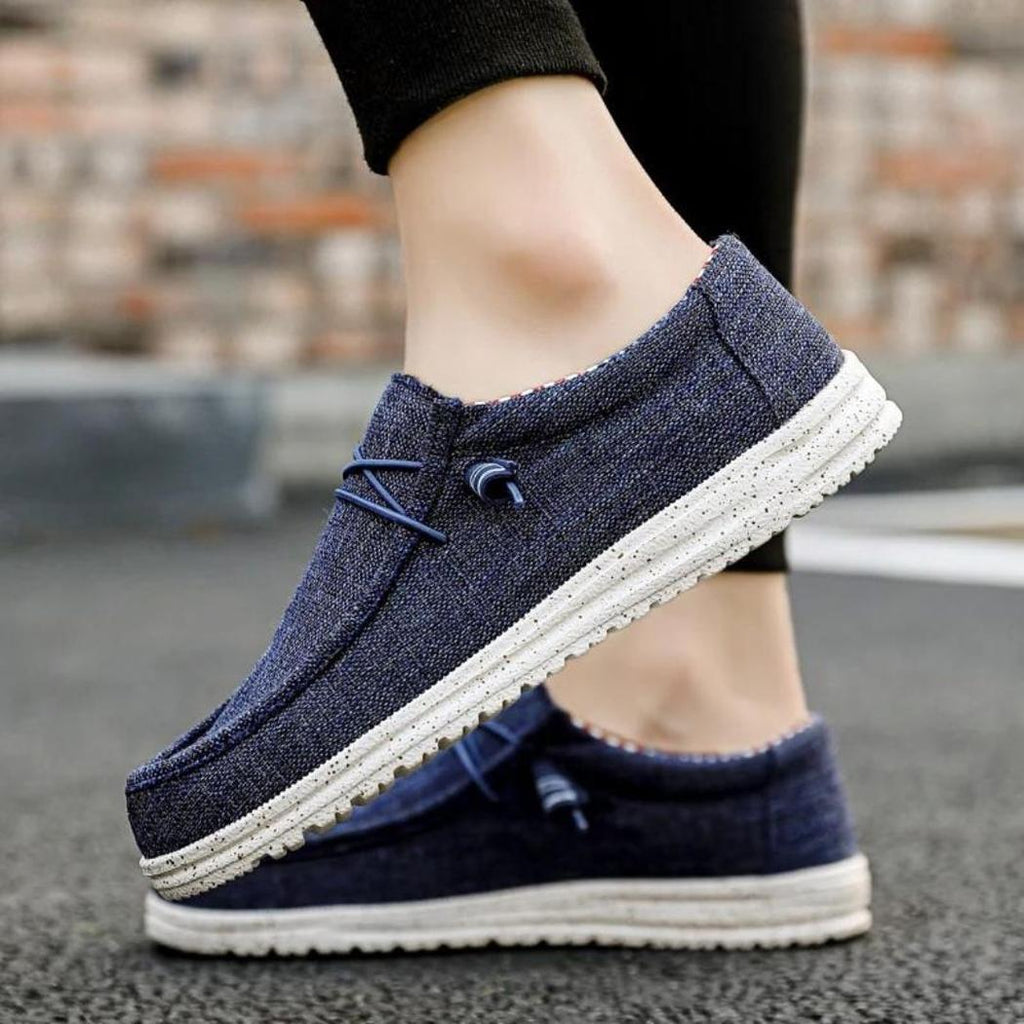 Je ziet een man met ontspannen blauwe loafers aan, alleen zijn voeten zijn zichtbaar