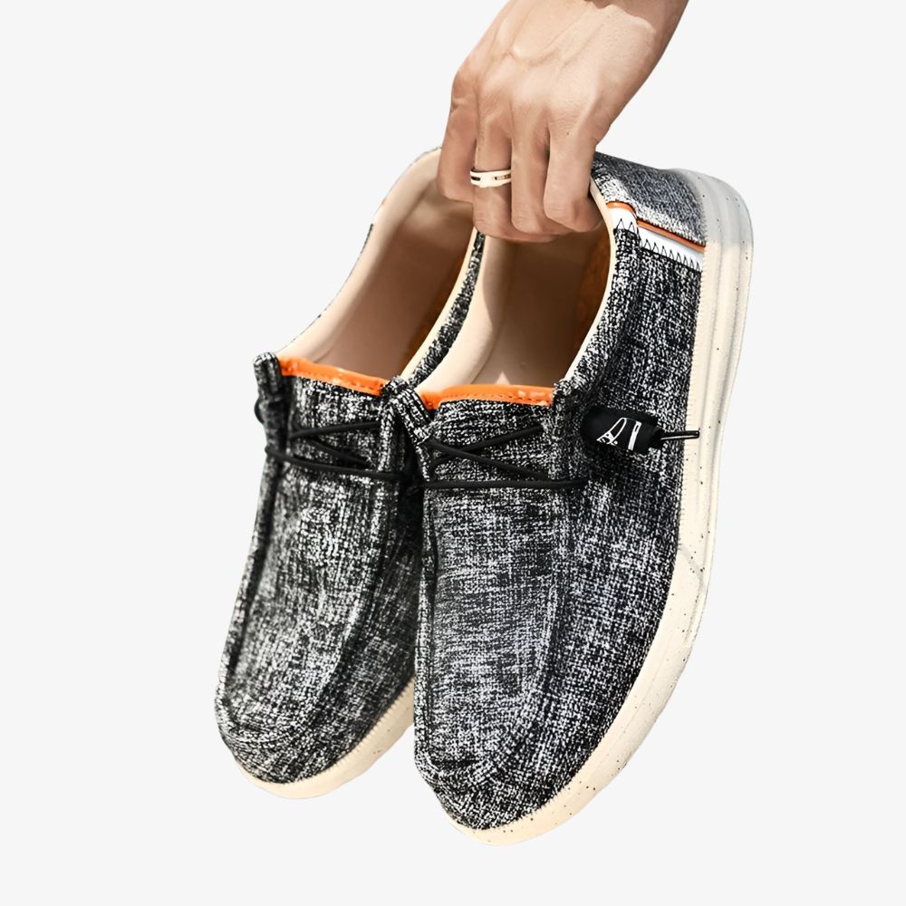 Paar canvas herenloafers in grijs met kleine zwarte vlekjes en een witte zool.