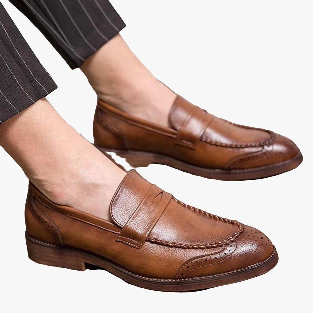 Je ziet een man zittend, je ziet zijn voeten en hij draagt bruine loafers