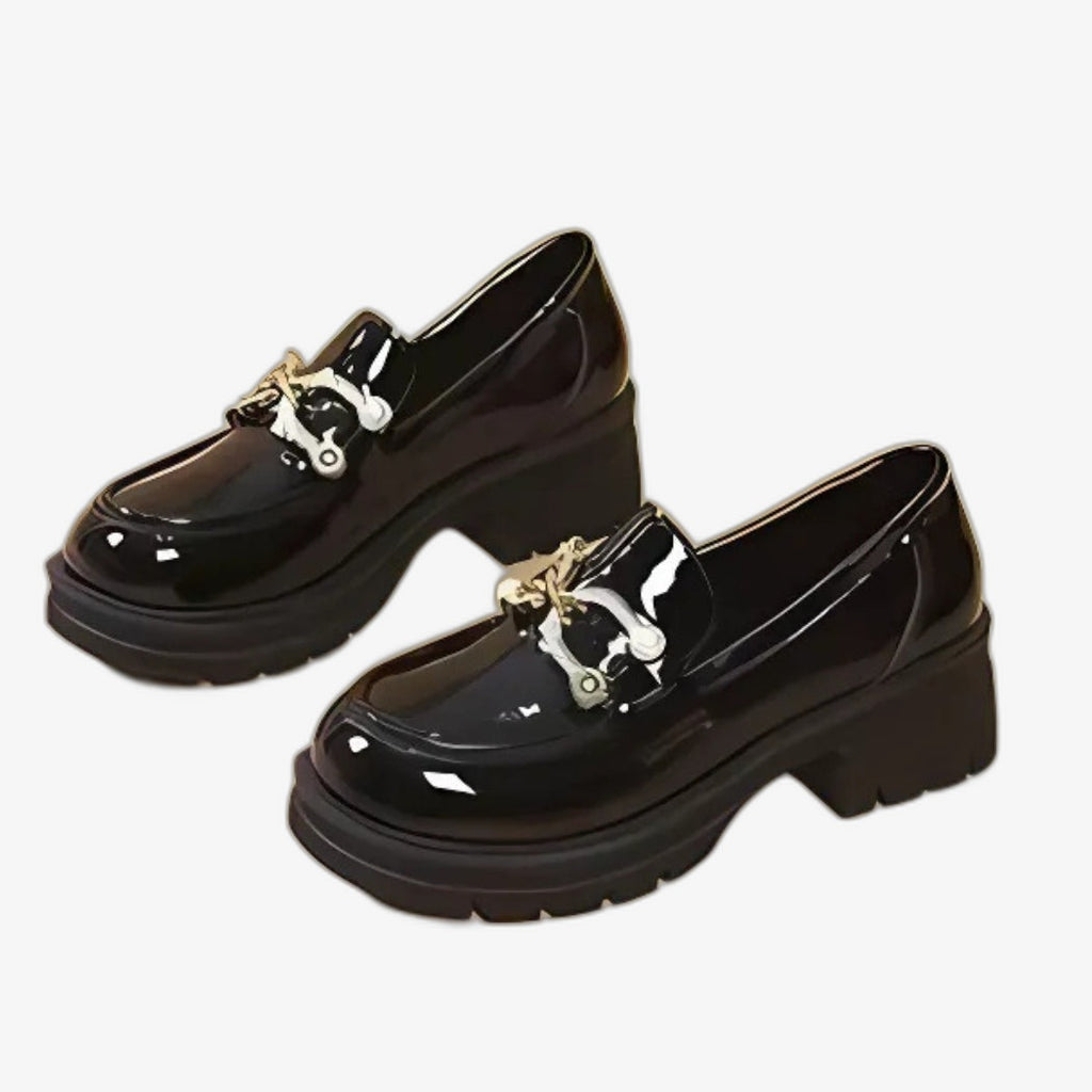 Zwarte gelakte damesloafers met een chique en moderne uitstraling. Ze hebben dikke hakken voor een mooie lijn en een goede stabiliteit, en zijn afgewerkt met een elegante zilverkleurige metalen gesp op de wreef, die hun glanzende design een verfijnd accent geeft.