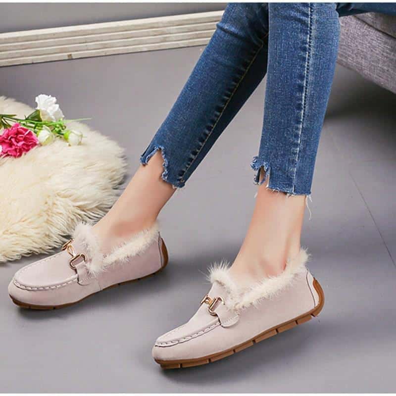 Paar beige suède winter loafers met zichtbaar bont, gedragen met jeans en hetzelfde model in zwart ernaast. De vloer is grijs en er ligt een kleed van beige bont op.