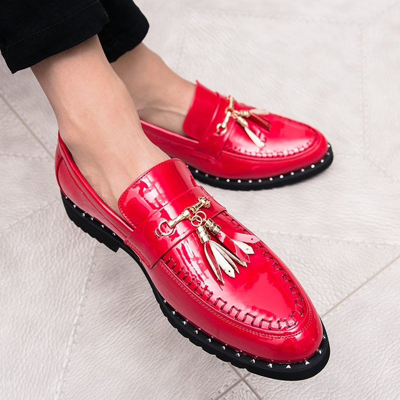 Felrode lakschoenen met decoratieve kwastjes aan de voeten van een man die in kleermakerszit een zwarte broek draagt.