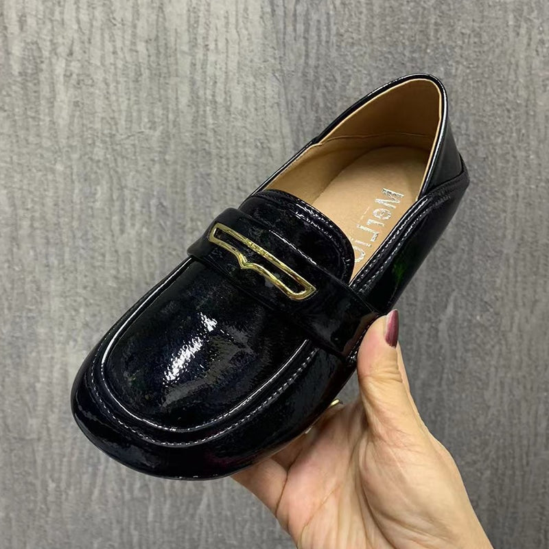 zwarte mocassin van synthetisch lakleer, met de hand gedragen op een grijze muur