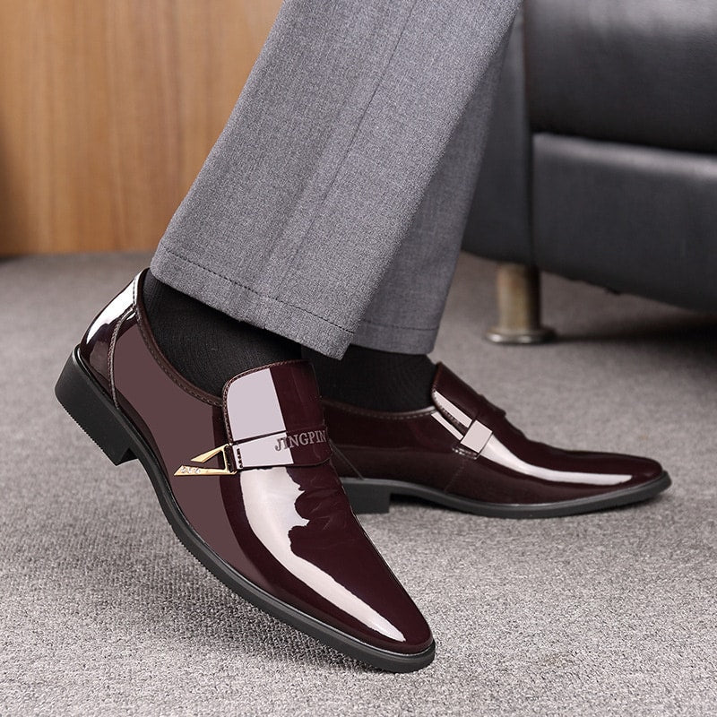 Voeten in bruine lakleren loafers en grijze broek op een grijs tapijt