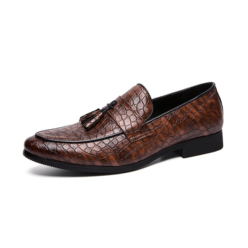 Een bruine slangenleren loafer met een band aan de bovenkant en decoratieve kwastjes, tegen een witte achtergrond.