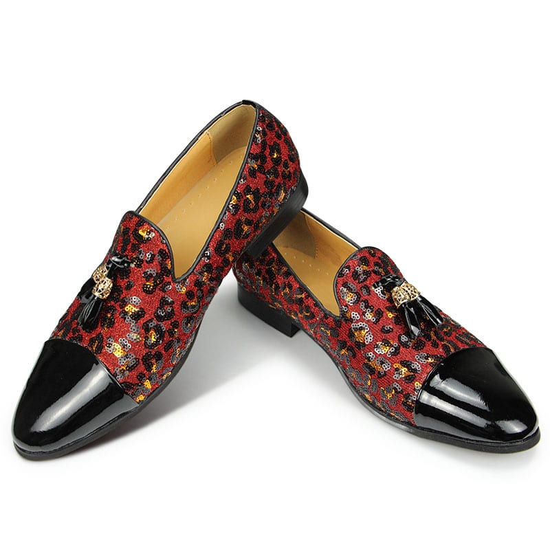 Op een witte achtergrond, een paar mocassins met een zwarte lak voorkant, de rest van de schoen in een luipaardprint pailletten in rood met kwastjes aan de bovenkant. De binnenkant is beige