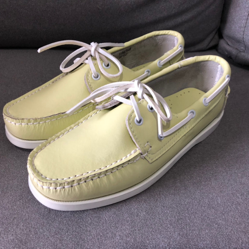Paar gele bootschoen-loafers met veters op een grijze vloer