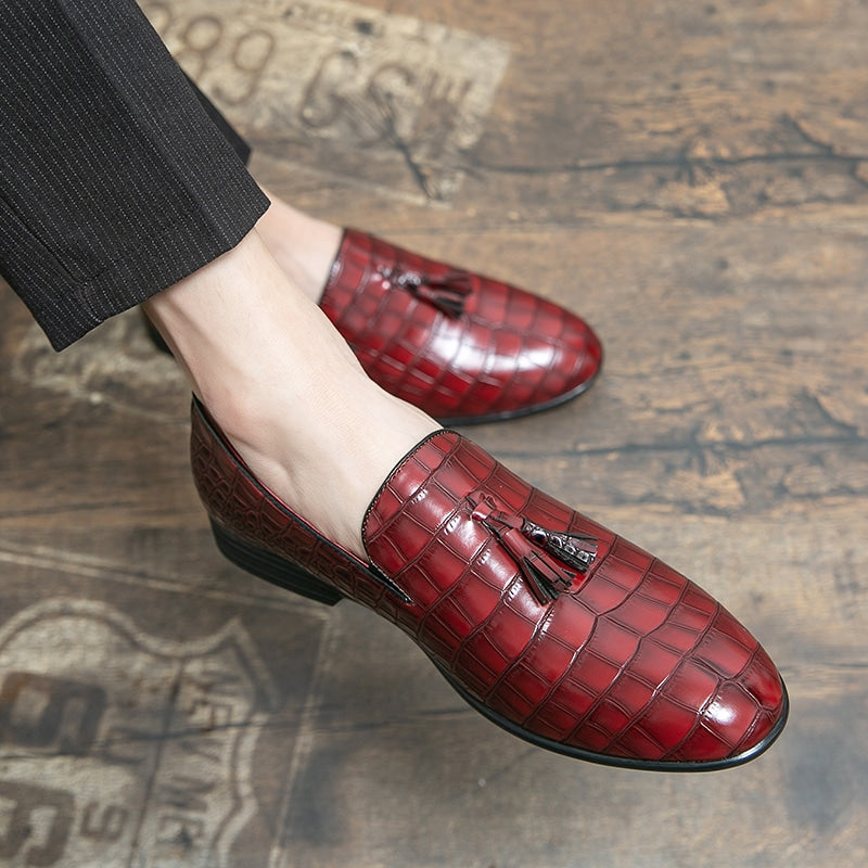 Voeten die rode mocassins met krokodilleneffect dragen met een kwastje bovenop de schoen