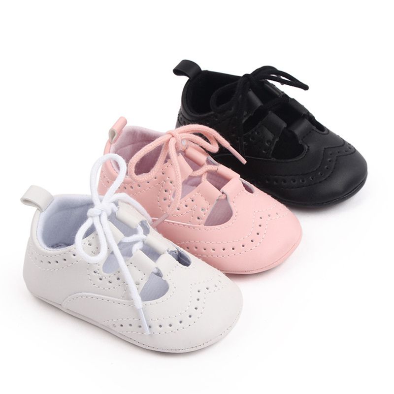 Drie baby mocassins met vetersluiting diagonaal op een rij in wit, roze en zwart