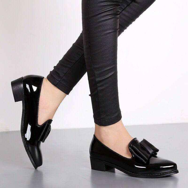 paar zwarte mocassins van synthetisch lakleer, gedragen, op een grijze vloer