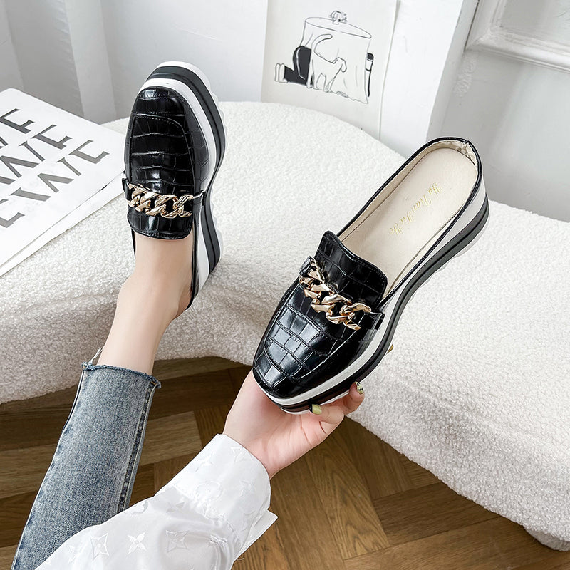 Vrouw naast een witte sofa die een mocassin vasthoudt en een zwarte mocassin aan haar linkervoet draagt