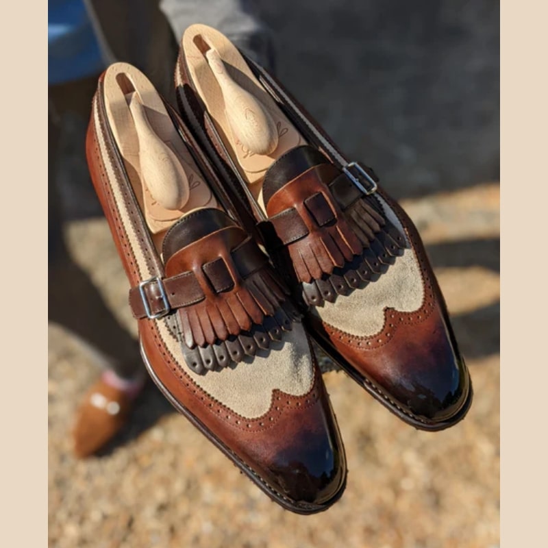 Een paar halfgepolijste mocassins van glad leer en bruin en beige synthetisch suède met tweekleurige franjes en riem- en gespsluiting bovenaan.