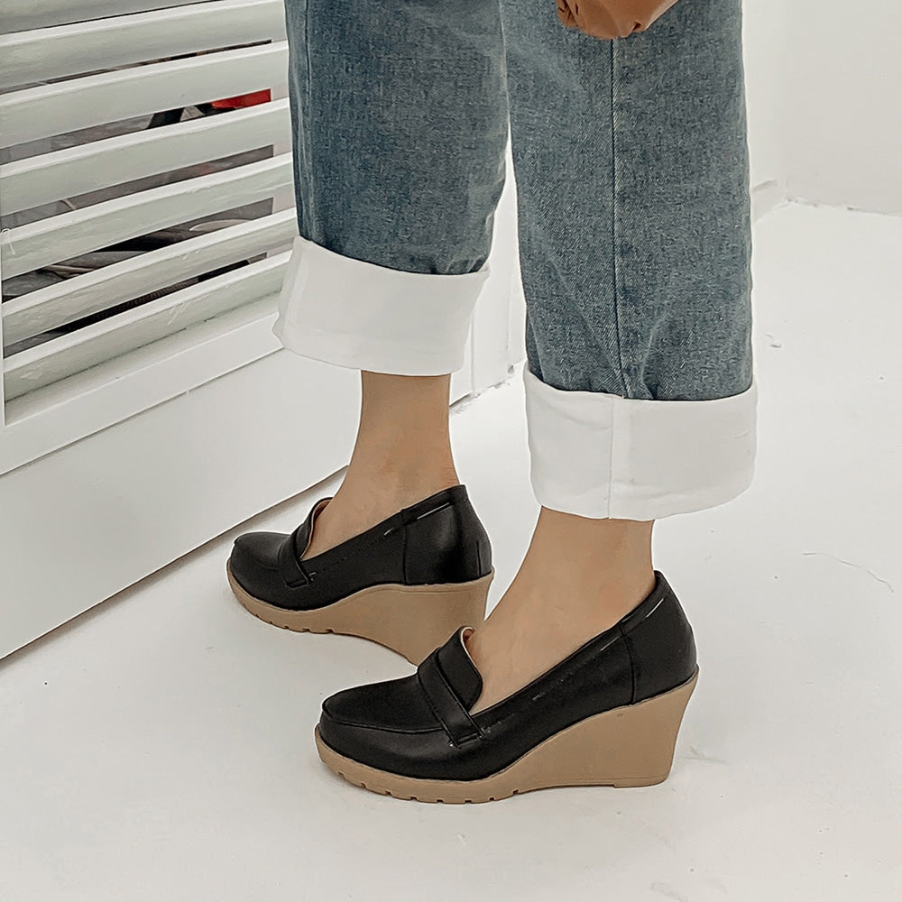 Foto van een paar zwarte sleehakken gedragen door een vrouw in jeans op een grijze vloer