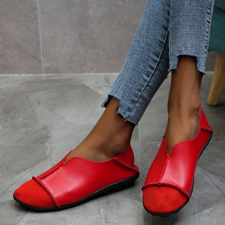 Paar zachte loafers met ronde neus in rood suède en glad leer met zichtbare stiksels gedragen met jeans op een lichtgrijze tegelvloer