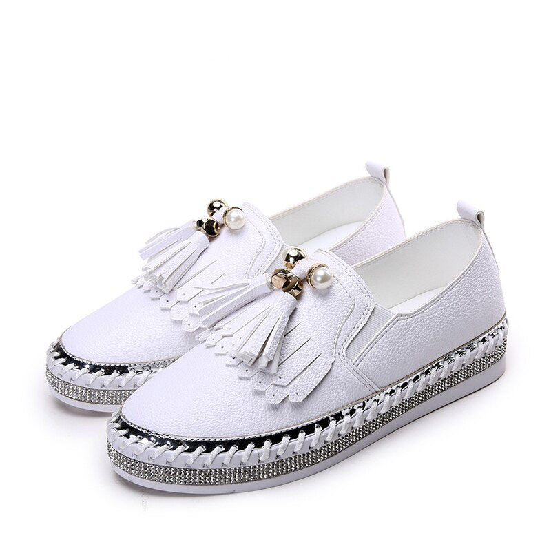 Paar witte mocassins met strass-steentjes en franjes aan de voorkant, op een witte achtergrond