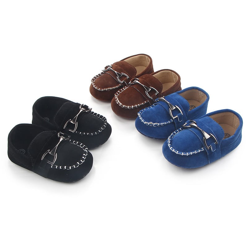 Op een witte achtergrond, 3 paar zachte zwarte, bruine en blauwe suède mocassins met zichtbare witte stiksels en een zilveren bit aan de bovenkant