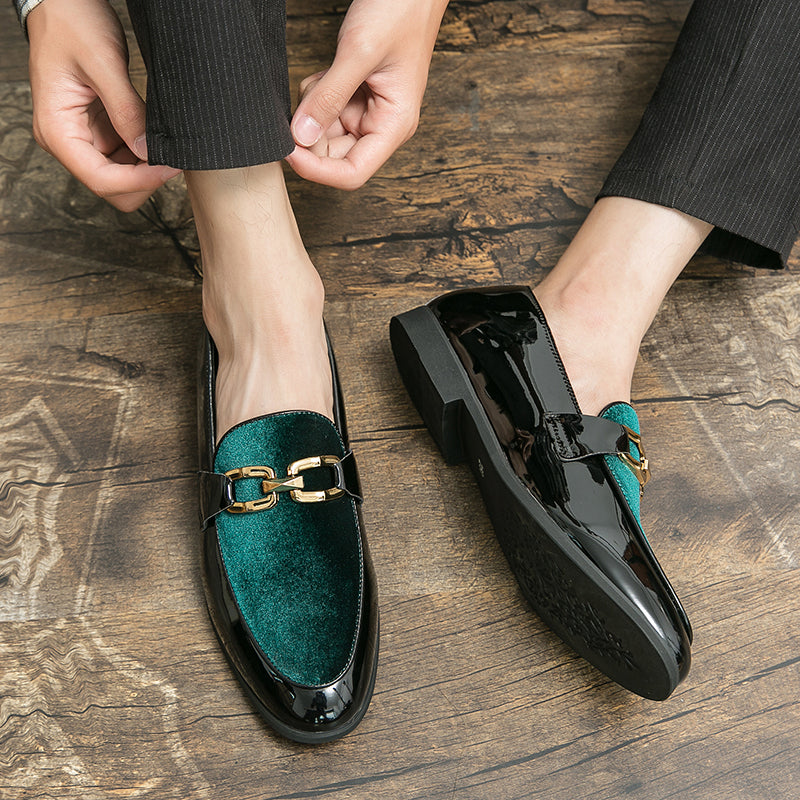 Paar mocassins voor heren in zwart lak op de beurt en glanzend groen fluweel met gouden bitje op de bovenkant. Ze worden gedragen met een zwarte broek op een bruine parketvloer
