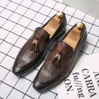 Leren loafers met een zigzagpatroon en decoratieve leren kwastjes met een goudkleurig metalen juk, donkere spitse tenen, op een wit met zwart geruite ondergrond.