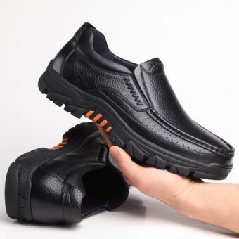 Foto van een paar zwarte leren orthopedische mocassins met dikke zolen. Eén schoen ligt op de grond, de andere wordt in één hand gehouden.