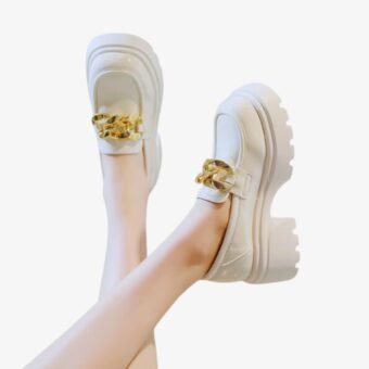 Witte loafer met dikke zwarte zool en gouden gespen op een witte achtergrond